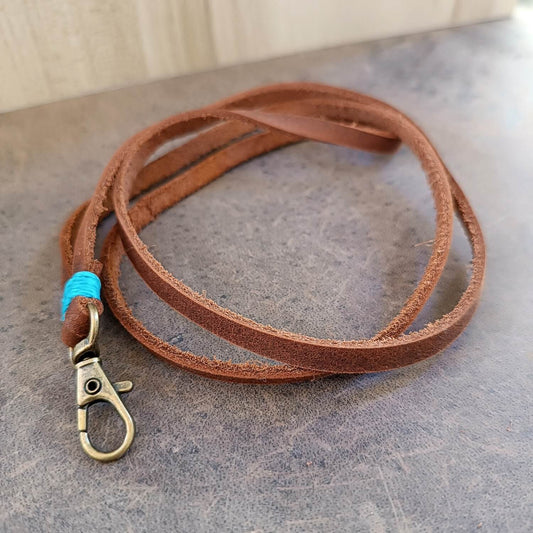 Brown leather lanyard with brass clasp on a gray surface