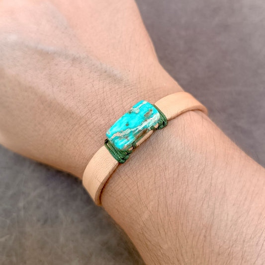 A close-up of a person's wrist wearing a tan leather wrap bracelet with a rectangular Imperial Jasper Stone.