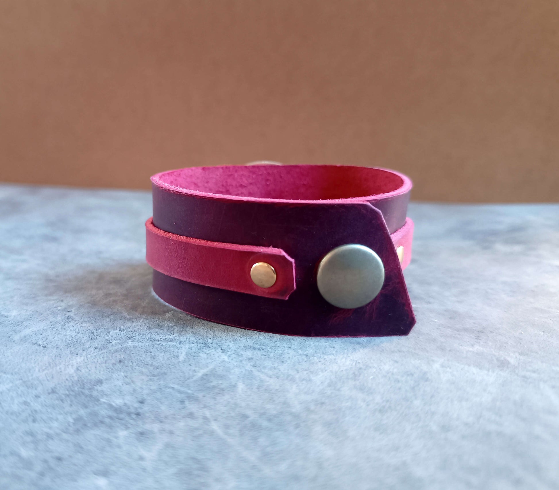 red leather bracelet with a silver button on a gray surface