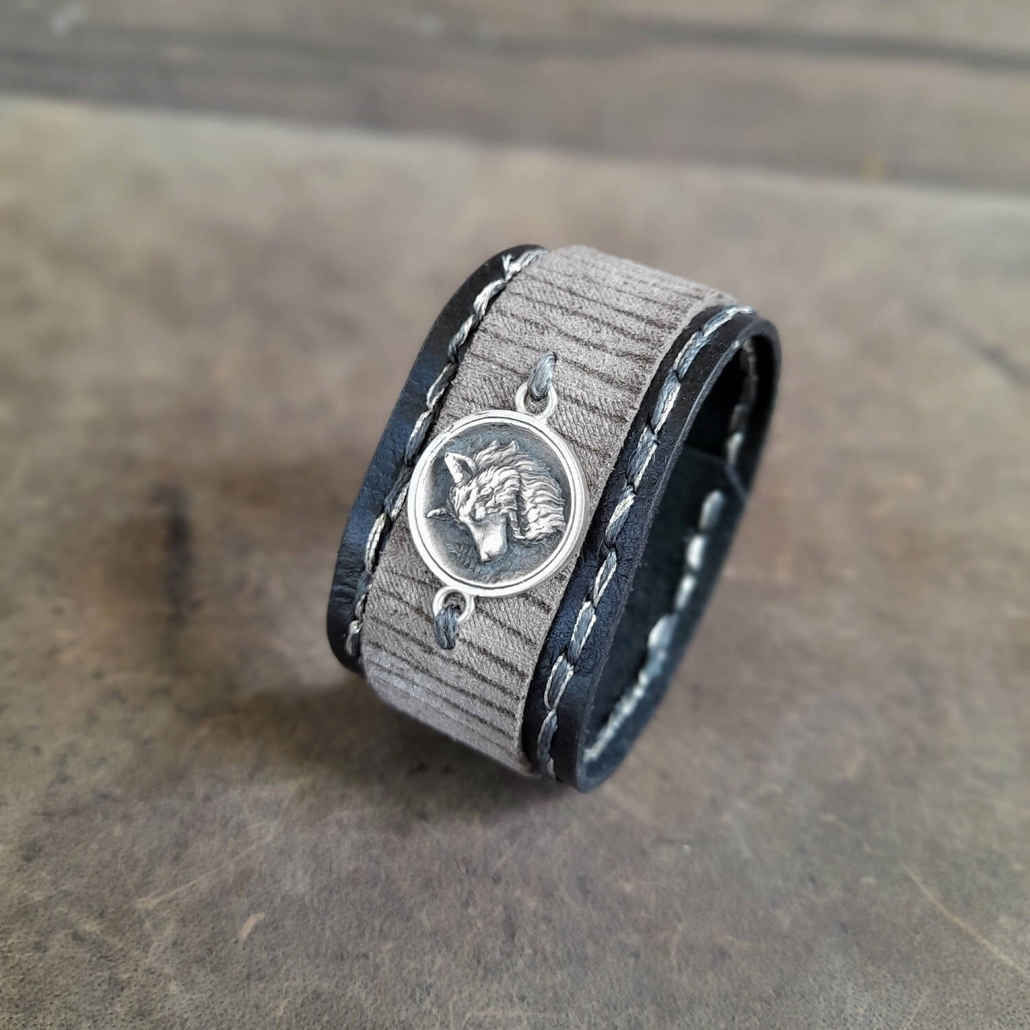 Leather bracelet with silver wolf pendant on a wooden surface