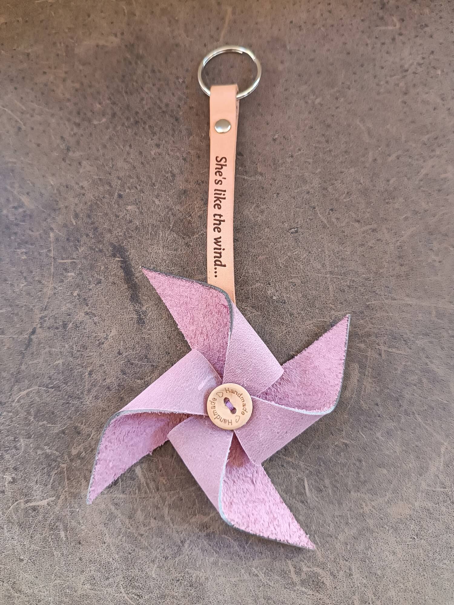 Pink pinwheel keychain with a leather strap and engraved text on a gray surface