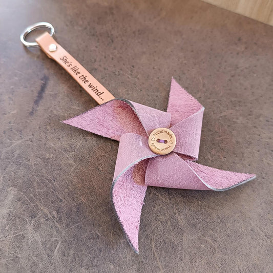 Pink leather pinwheel keychain with a leather strap on a textured surface