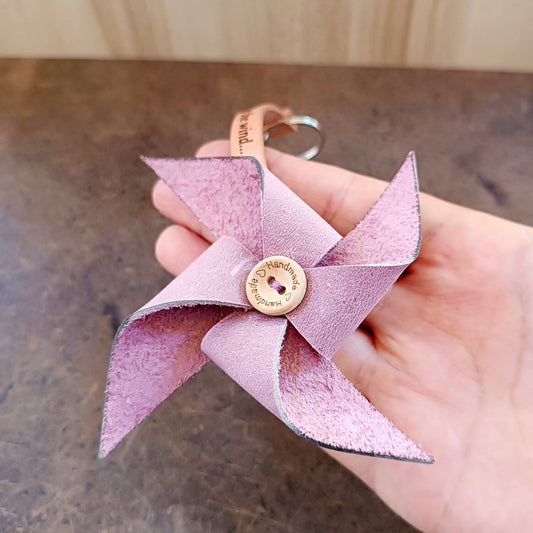 Pink leather keychain shaped like a pinwheel held by a hand on a wooden surface