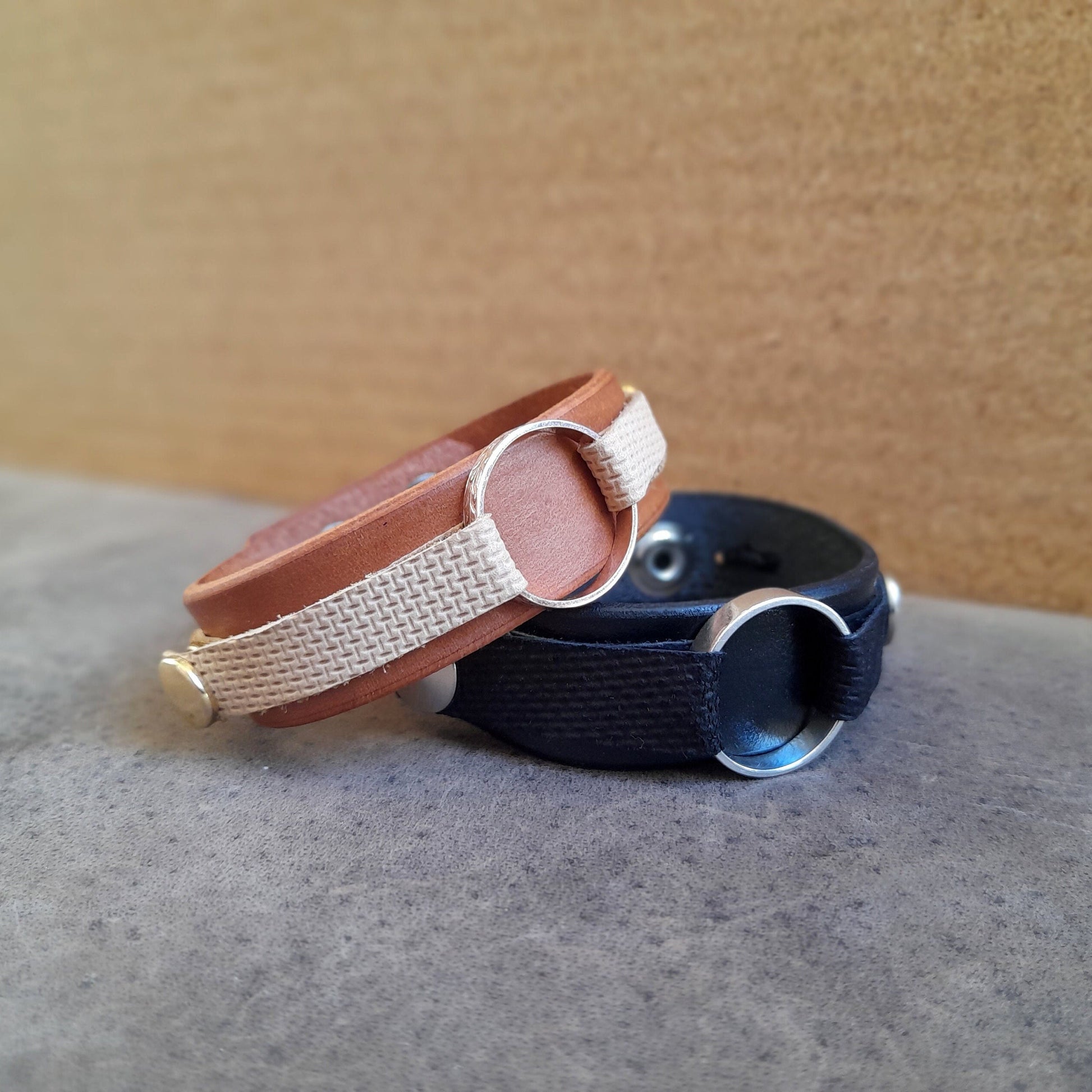 Leather Ring Holder Bracelets in mustard brown and black full-grain crazy horse leather, showing snap buttons and ring loop on flat surface.