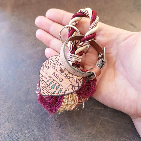 Heart-shaped keychain with braided design and 'Mina' engraving held in a hand.