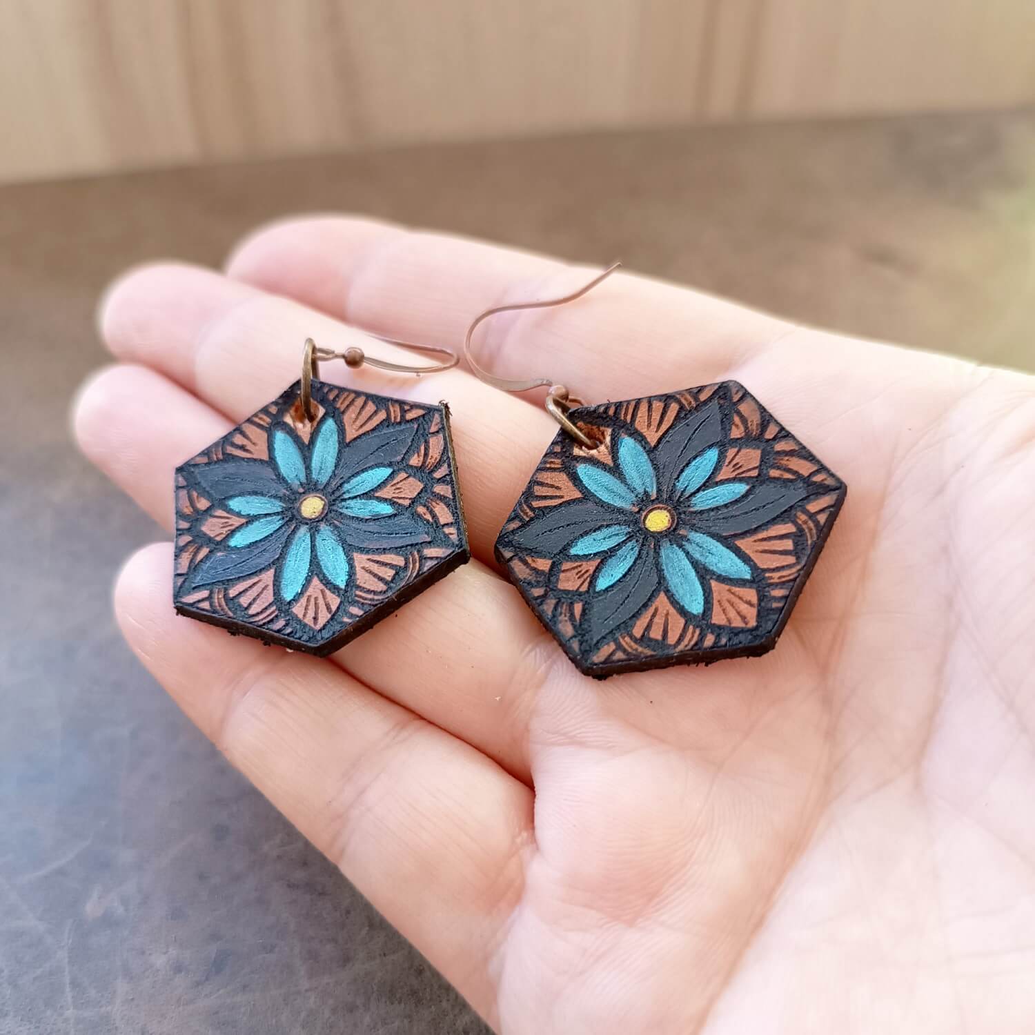 Hexagonal earrings with floral design held in a hand against a neutral background