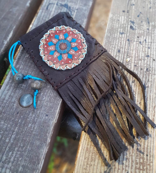A small dark brown leather pouch with a hand-painted mandala design in blue and red, adorned with fringe and a drawstring closure.