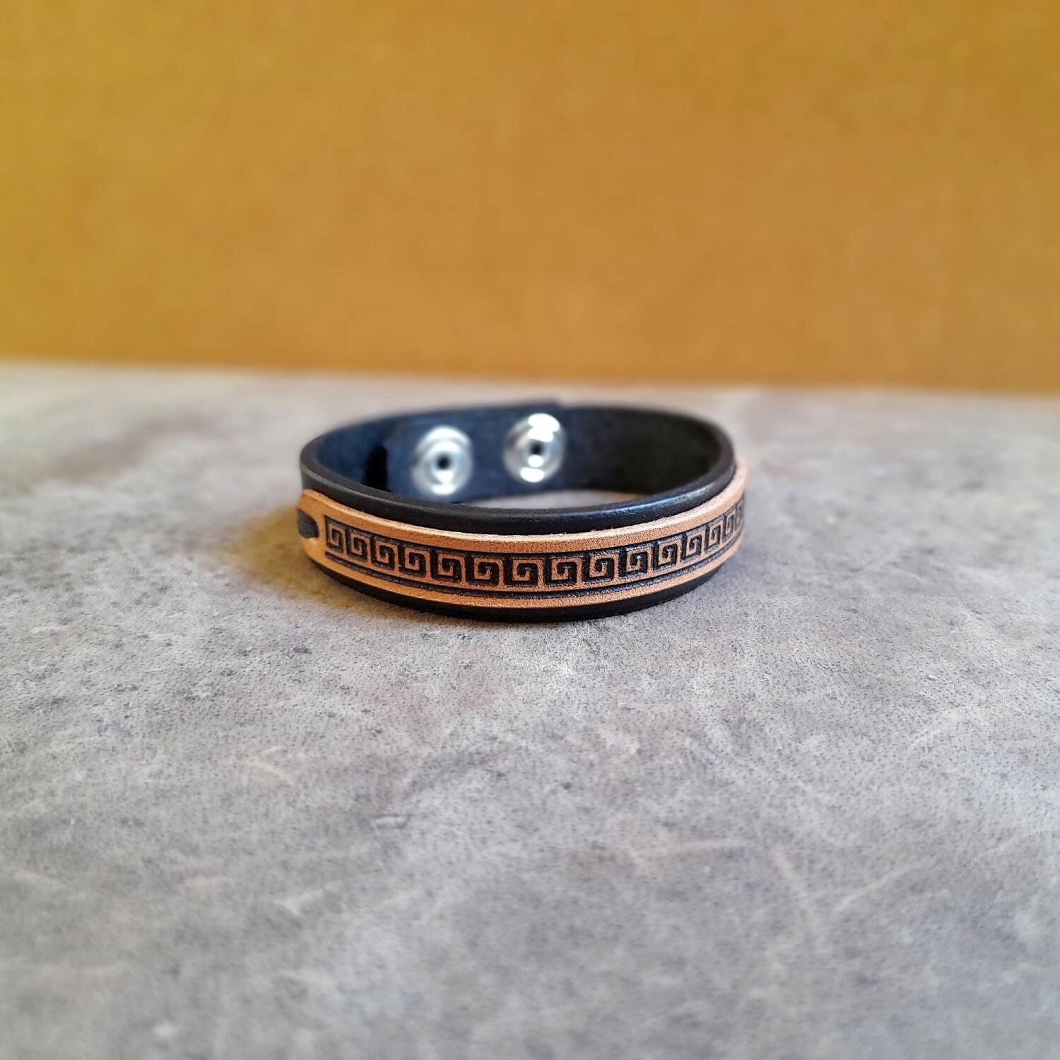 Slim black leather cuff showing engraved Greek meander design and full grain leather texture