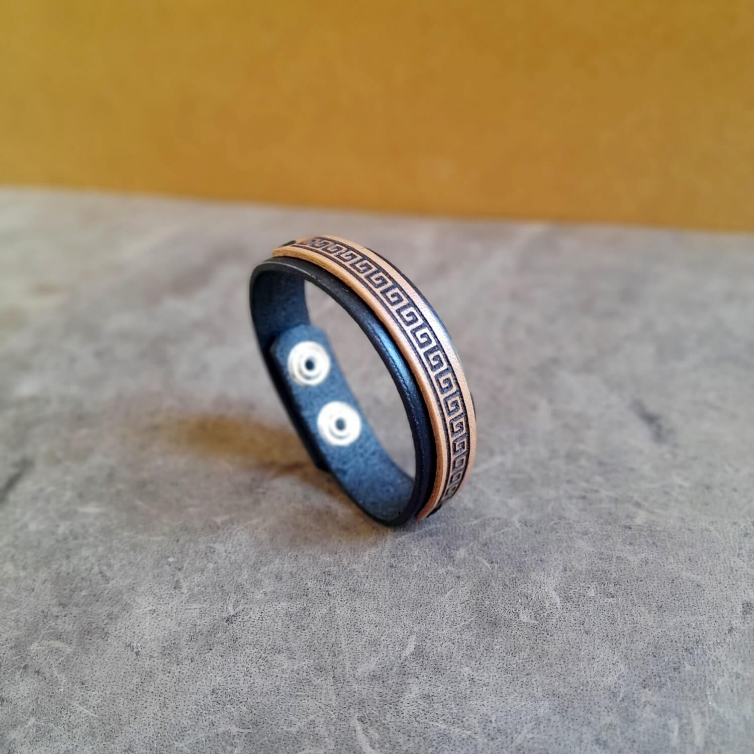 Minimalist black leather bracelet with engraved Greek meander symbol on front view, flat