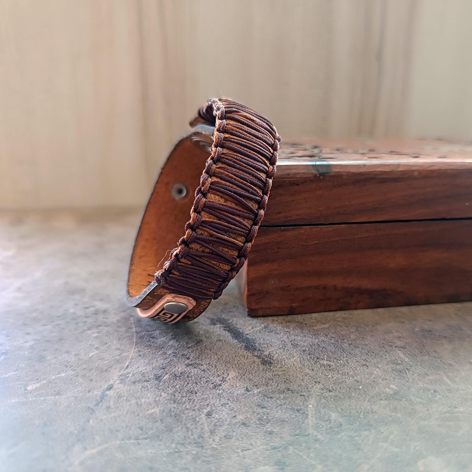 Brown leather bracelet with thick macrame knotting on a wooden surface with a neutral background