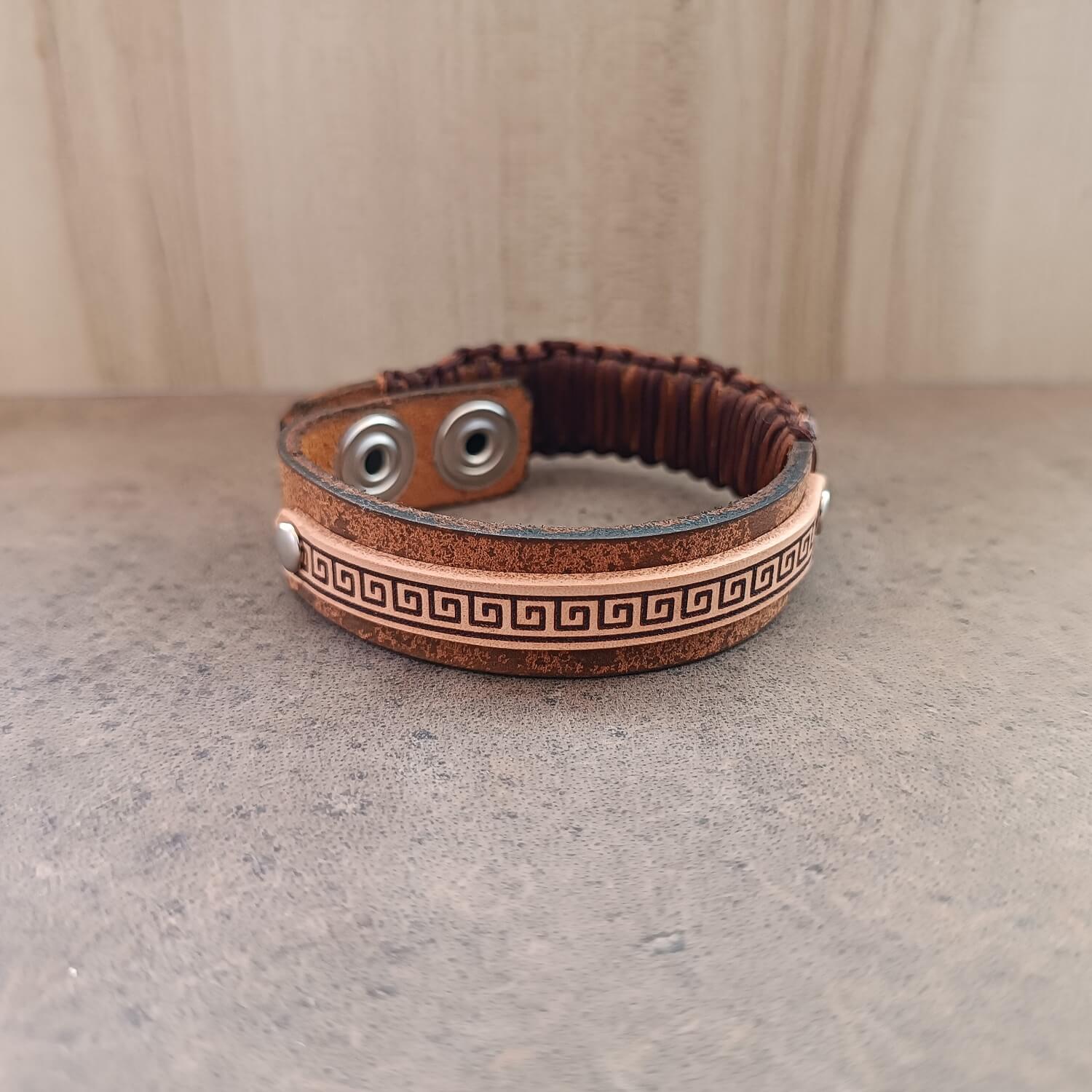 Brown leather bracelet with decorative greek key (meander) pattern on a neutral background