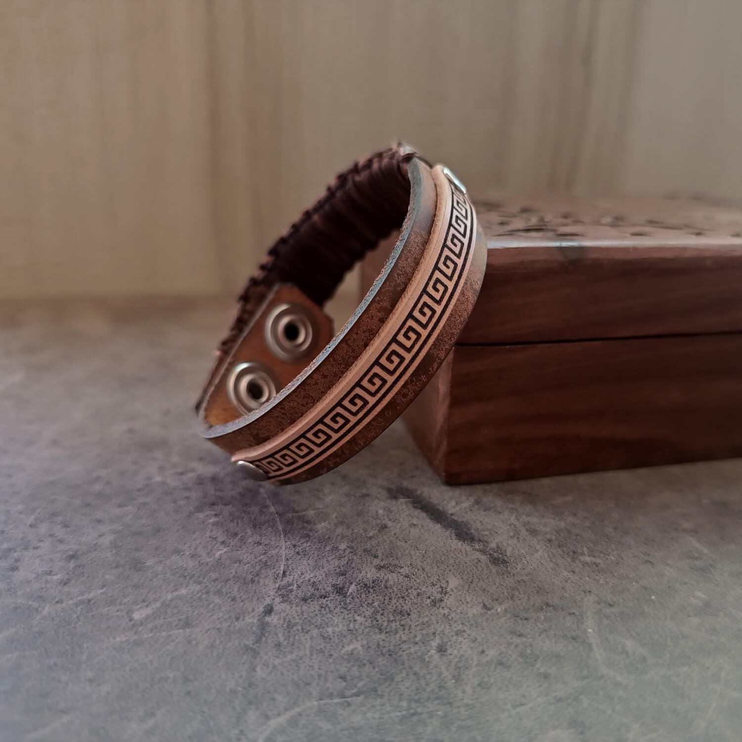 Brown leather bracelet with decorative meander pattern and macrame on a textured surface