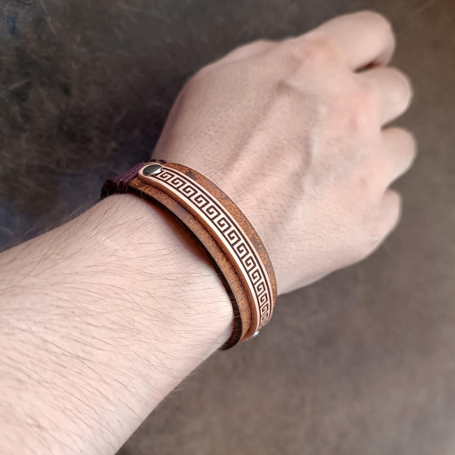 Brown leather bracelet with meander pattern on a wrist against a neutral background