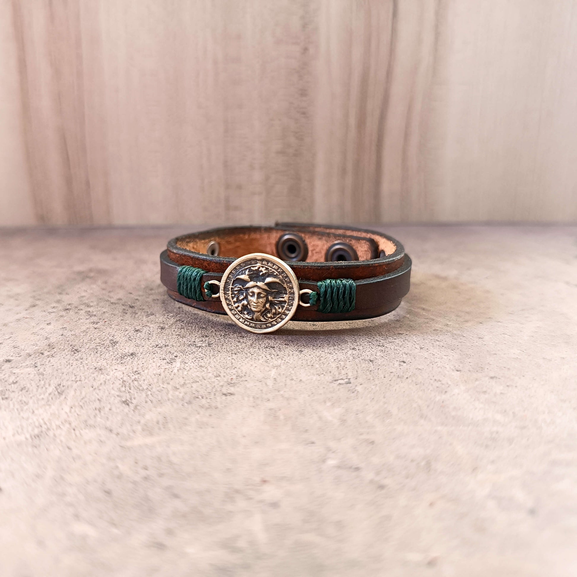 Brown leather bracelet with a Medusa pendant on a beige surface