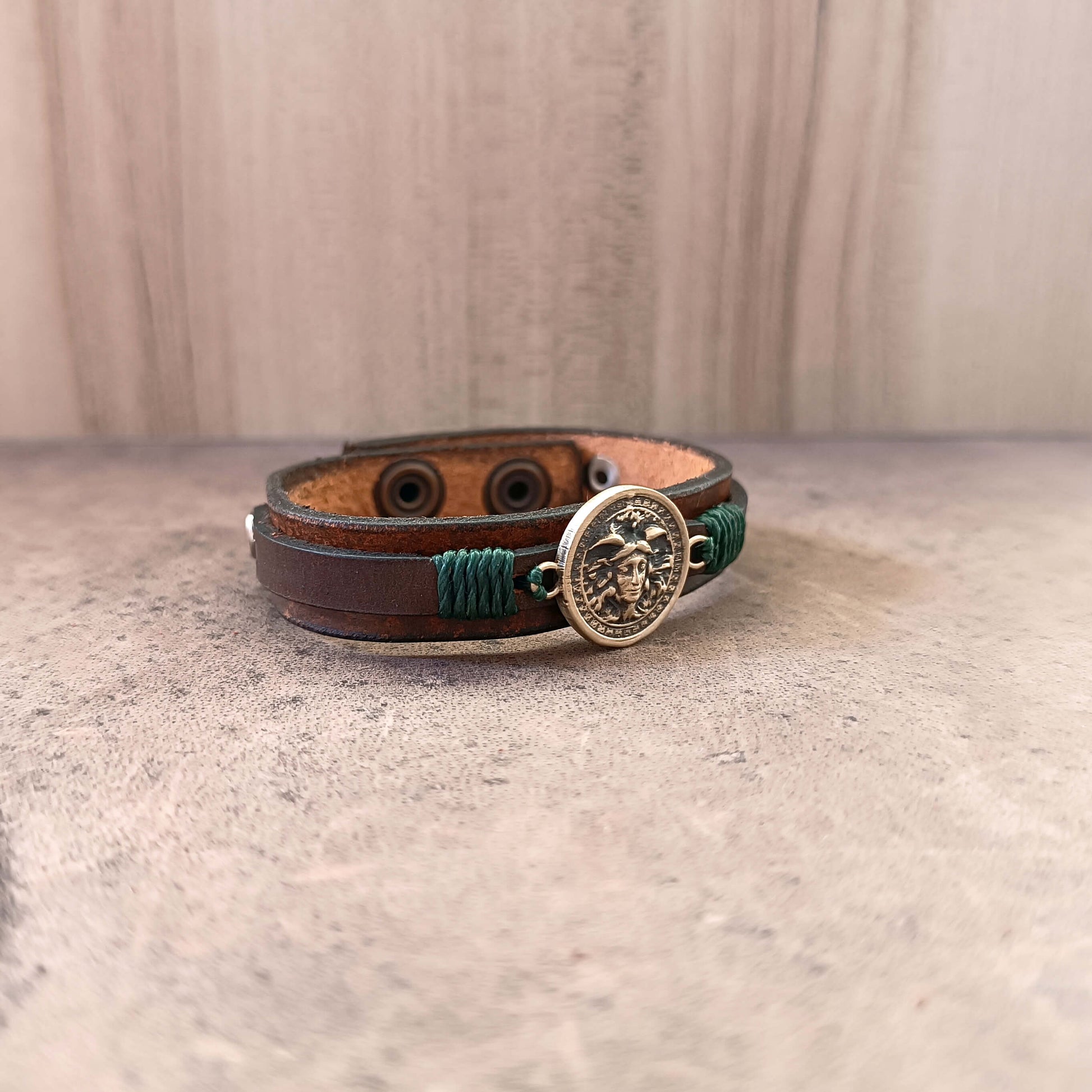 Brown leather bracelet with medusa pendant  on a beige surface, side view