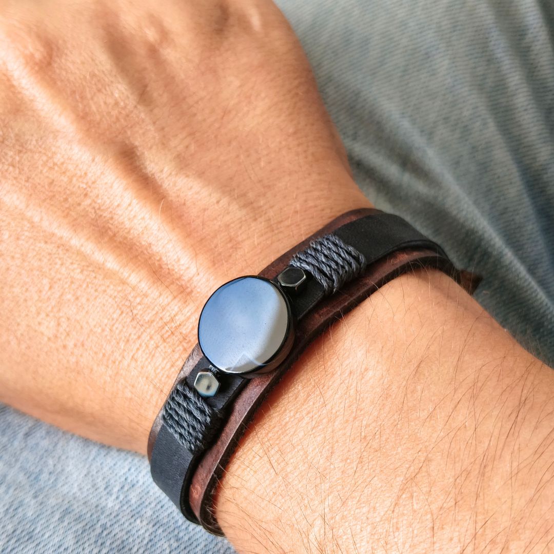 A close-up of a person's wrist wearing a dark brown leather wrap bracelet with a round black agate.