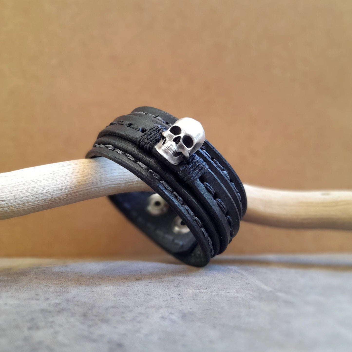 Men's black full-grain leather cuff with a prominent solid sterling silver 3D skull, main side view.