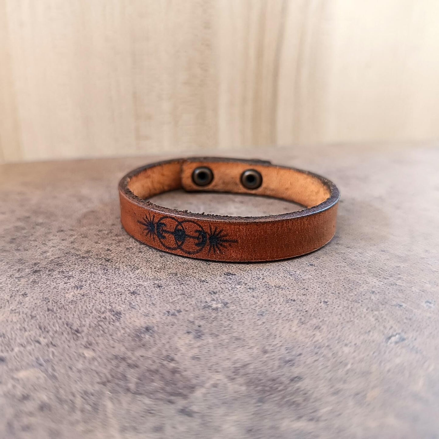 Brown leather bracelet with black engraved vesica piscis design on a textured surface