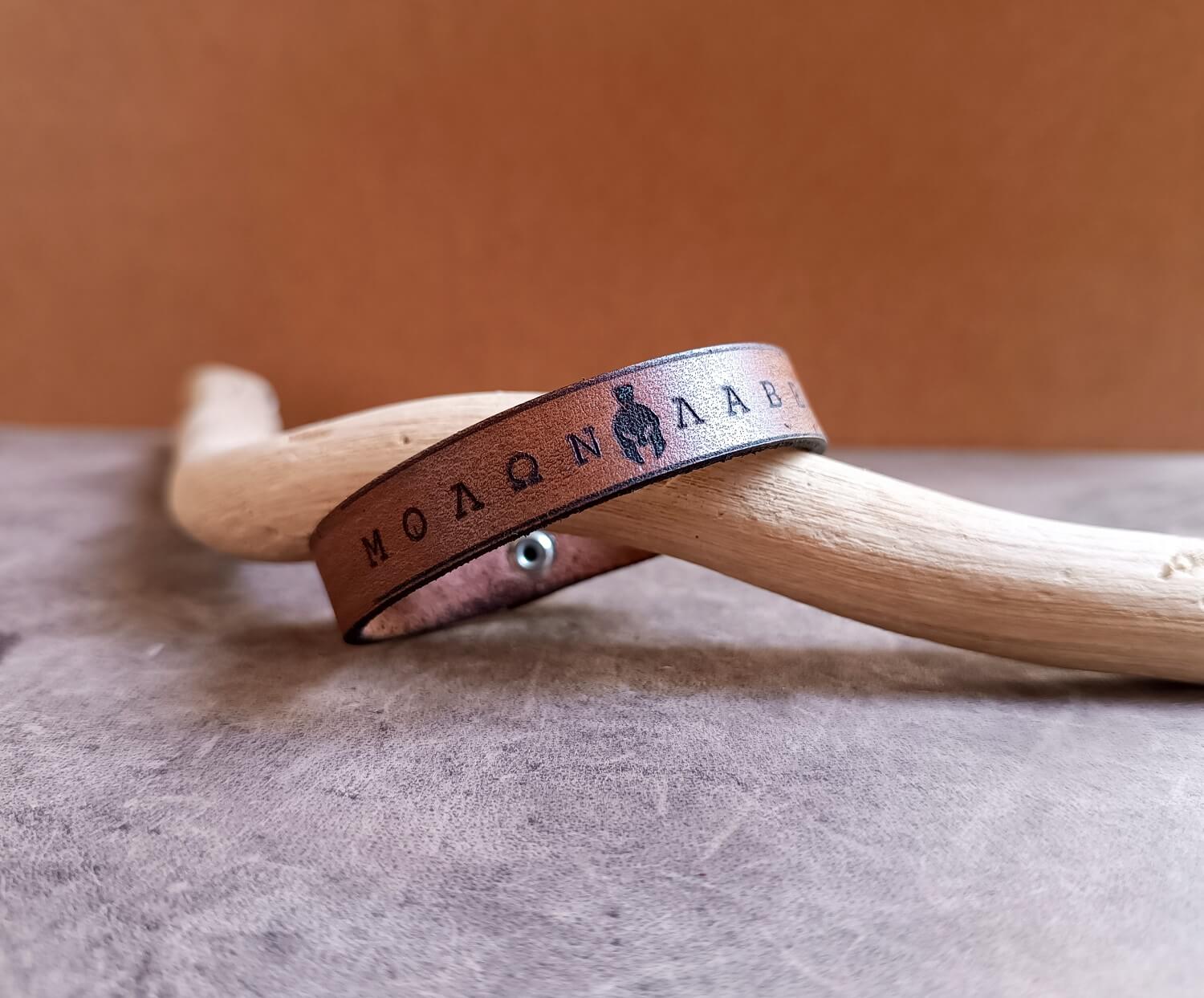 Brown leather bracelet with engraved text on a wooden surface