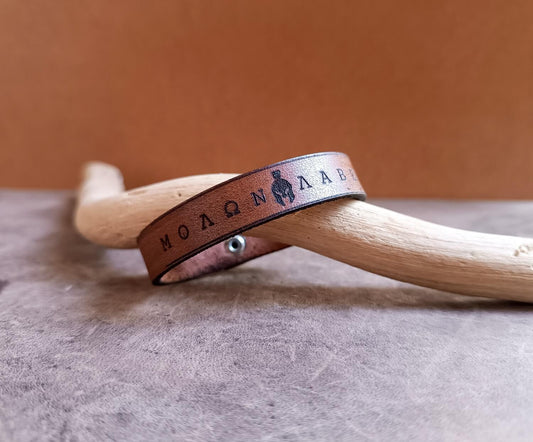 Brown leather bracelet with engraved text on a wooden surface