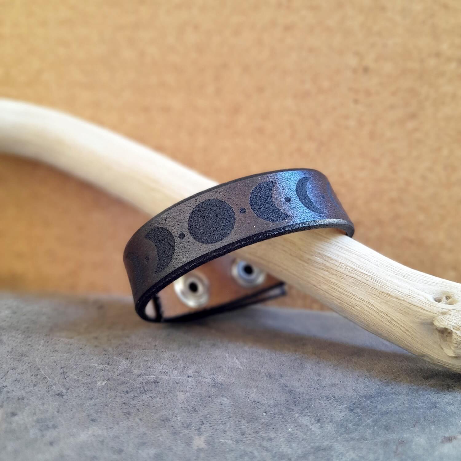 Dark Brown leather bracelet with moon phase engraved design on a driftwood