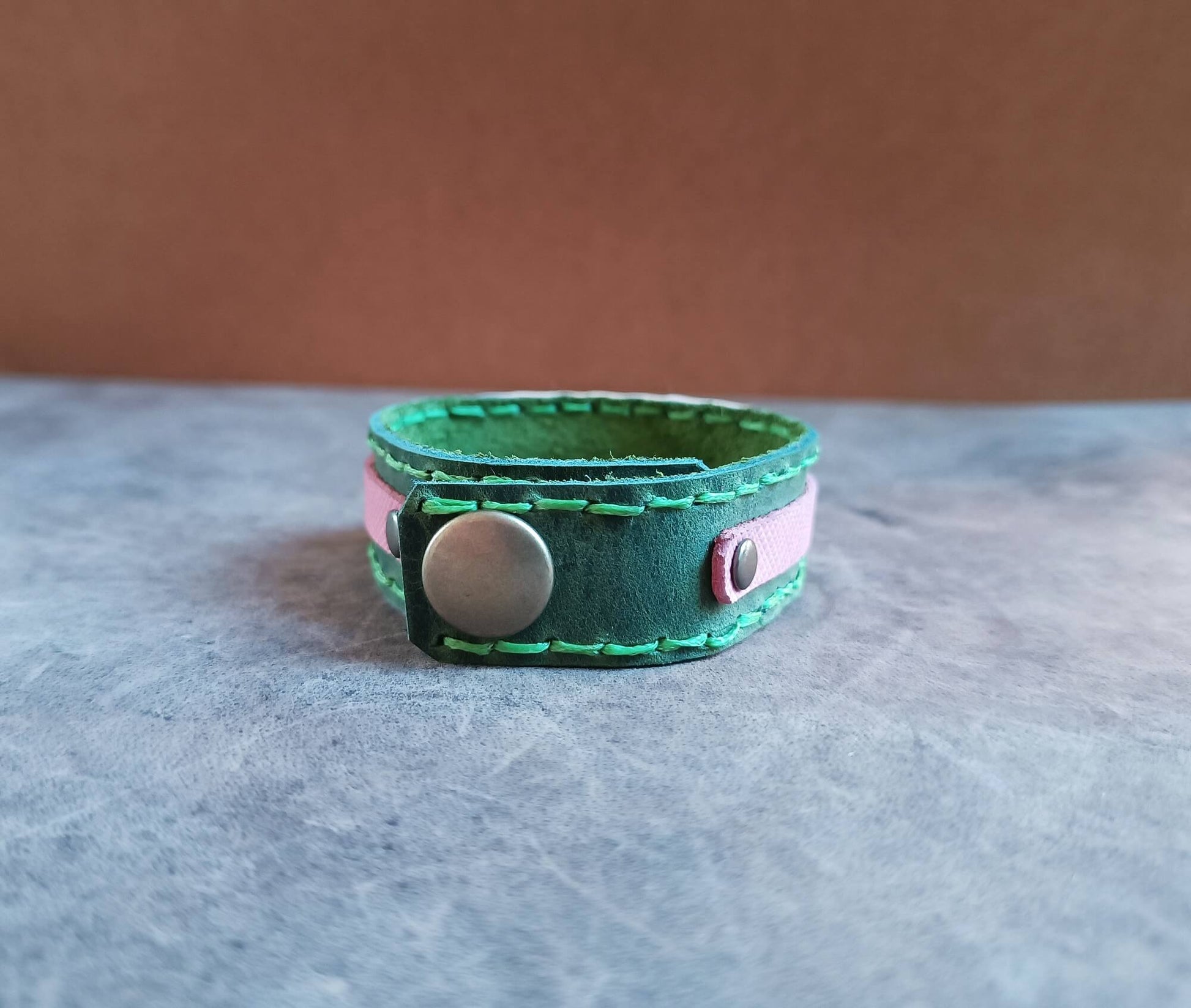 Green leather bracelet with a button clasp on a gray surface
