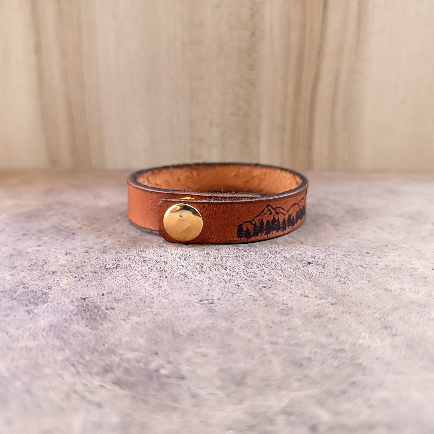 Brown leather bracelet with a gold button on a textured surface