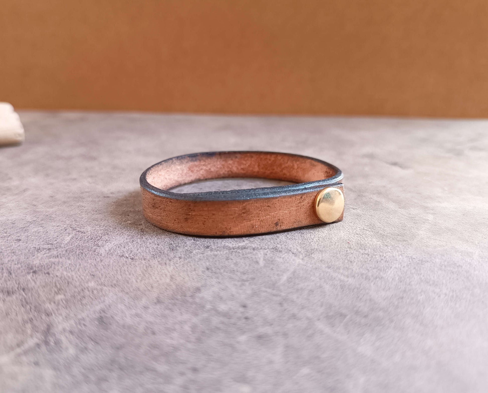 Brown leather bracelet with a gold accent on a gray surface
