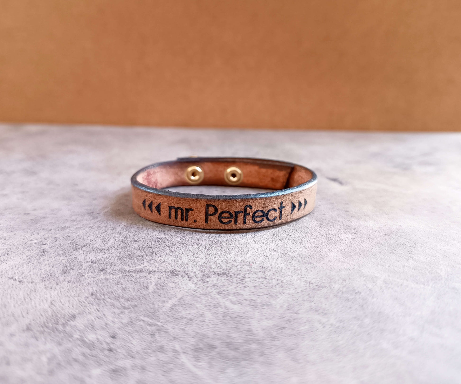 Leather bracelet with 'mr. Perfect' engraving on a gray surface
