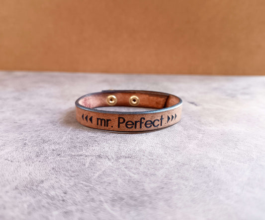Leather bracelet with 'mr. Perfect' engraving on a gray surface