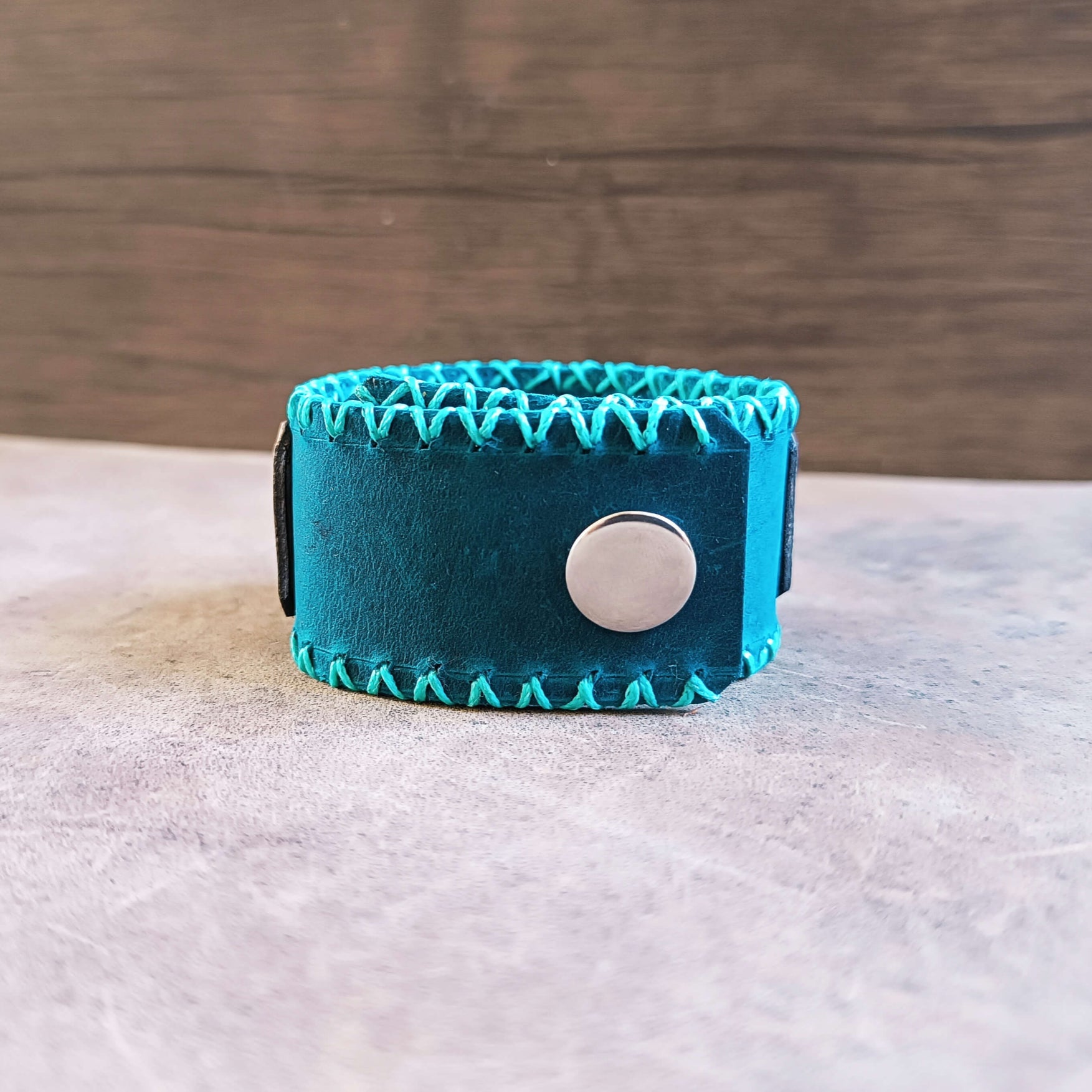 Teal leather bracelet with a silver button on a wooden surface