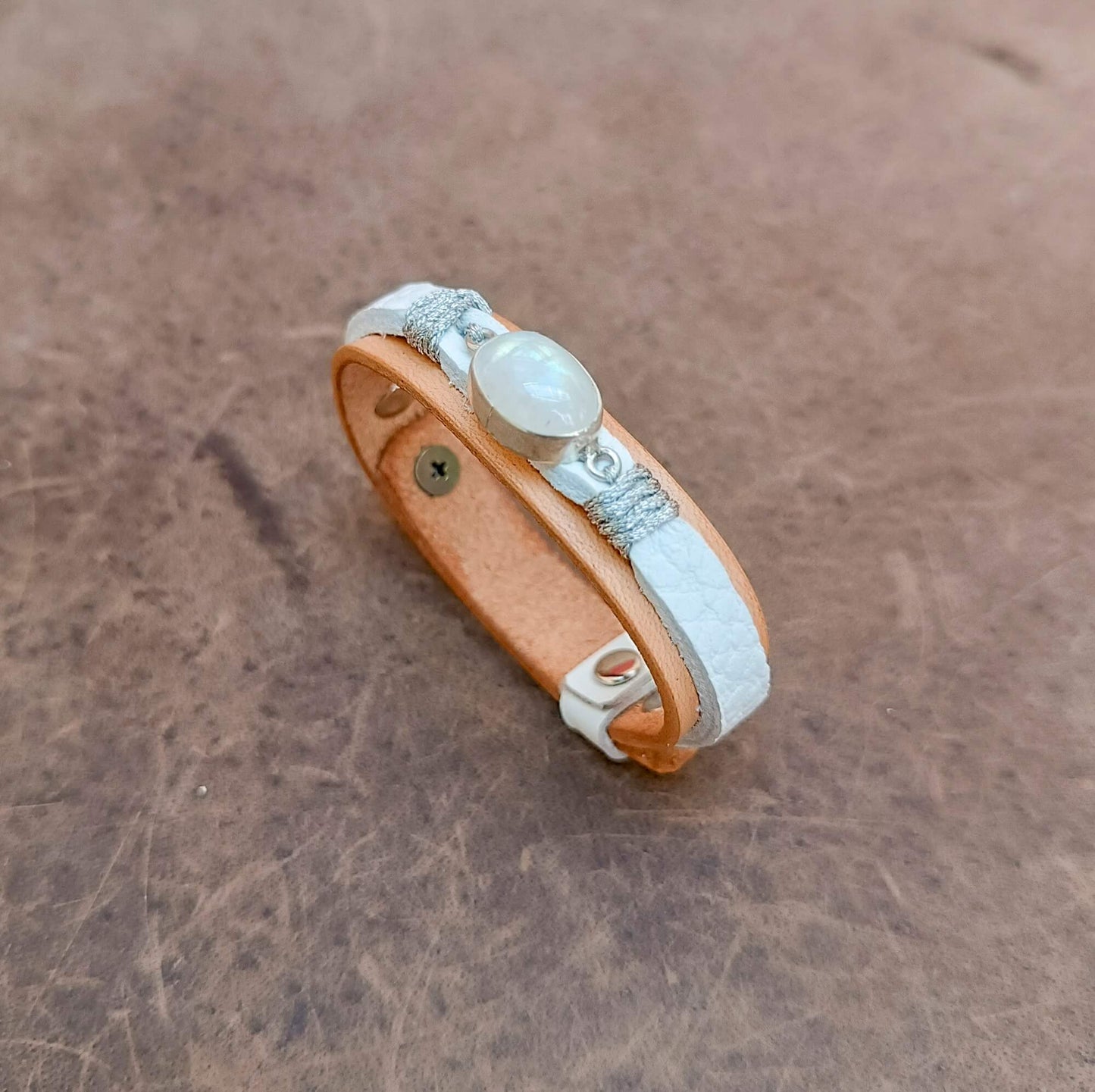A handcrafted one-of-a-kind women's leather bracelet featuring a hand-cut natural moonstone set in sterling silver on raw untreated vachetta leather, angle view
