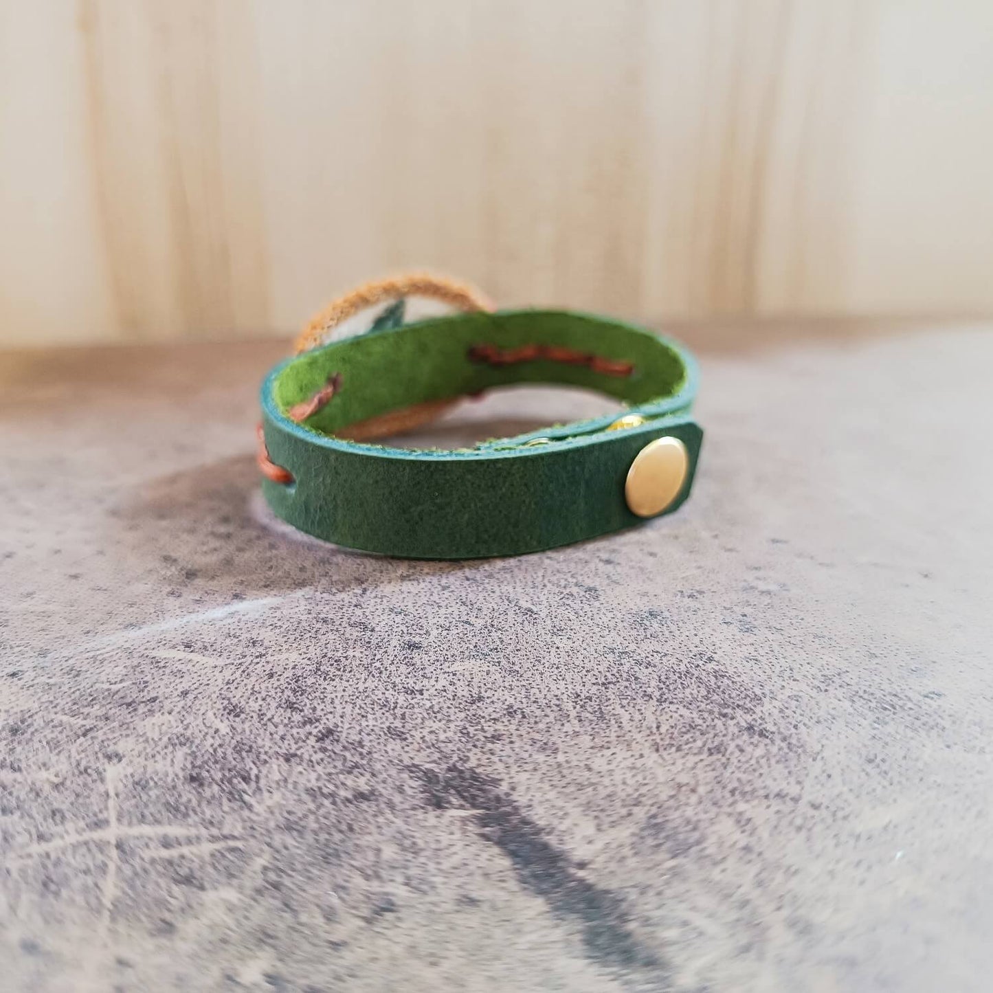 Green leather bracelet with a gold button clasp on a textured surface