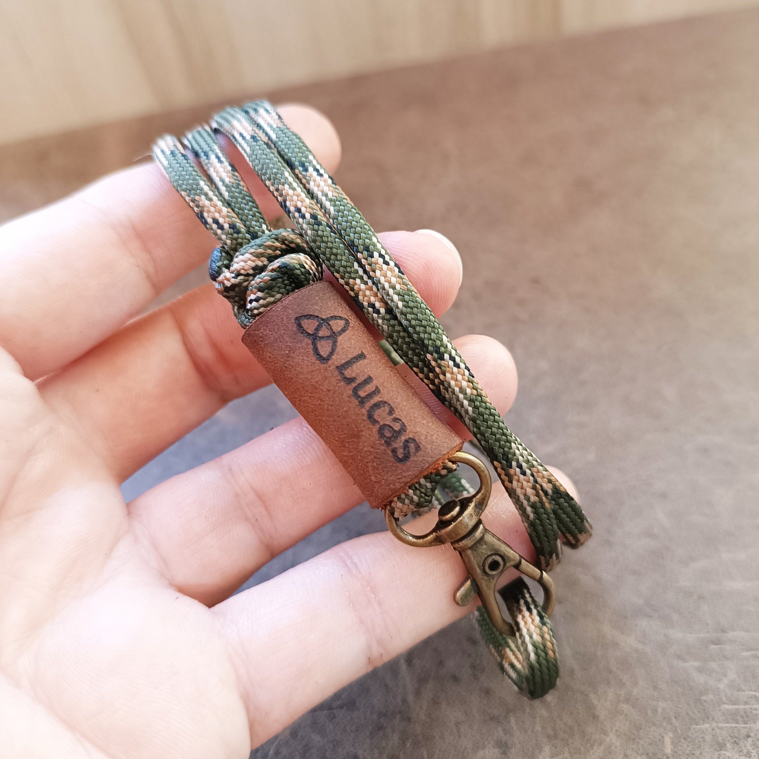 Hand holding a camouflage paracord keychain with a leather tag labeled 'Lucas'.