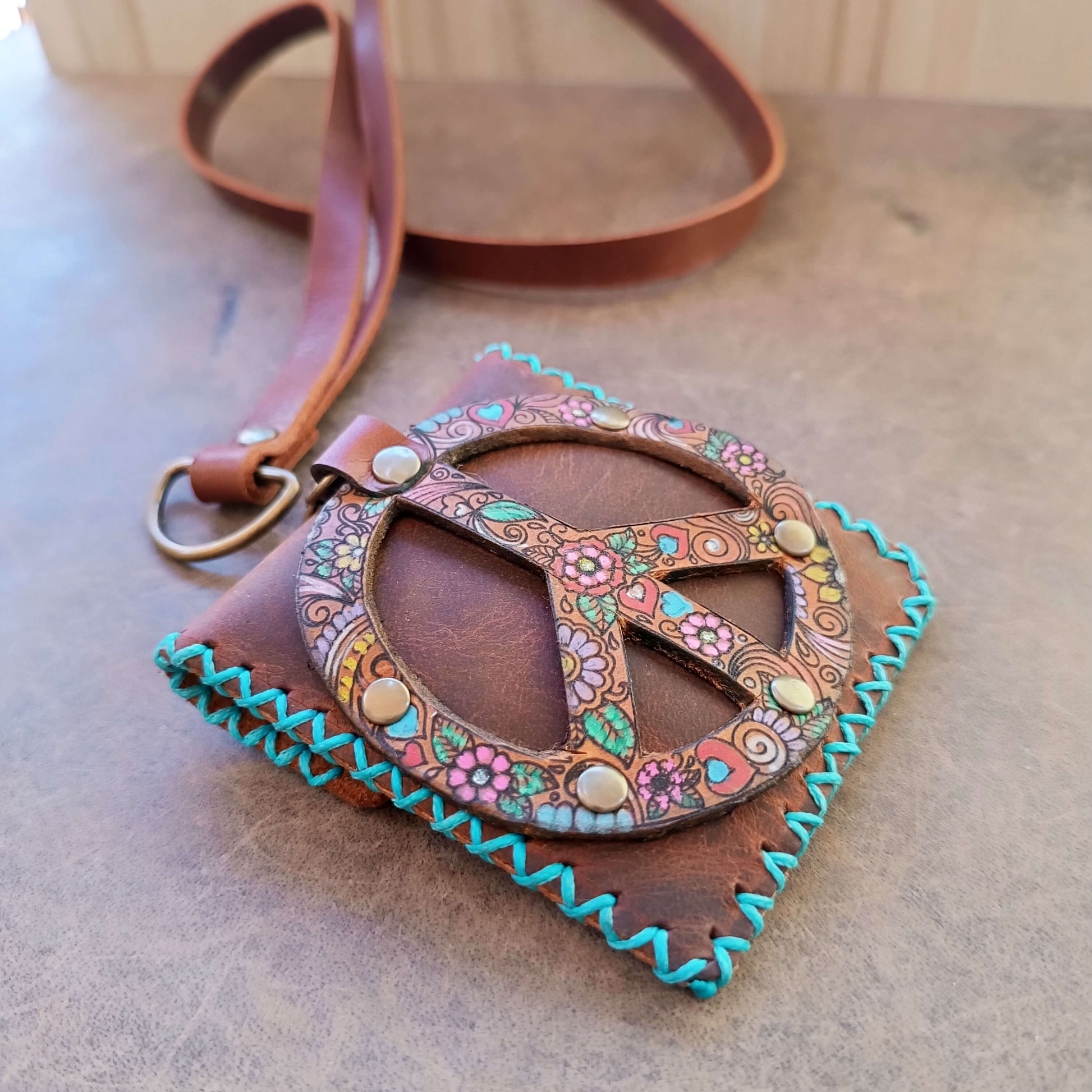 Brown leather bag with floral peace symbol design on a wooden surface