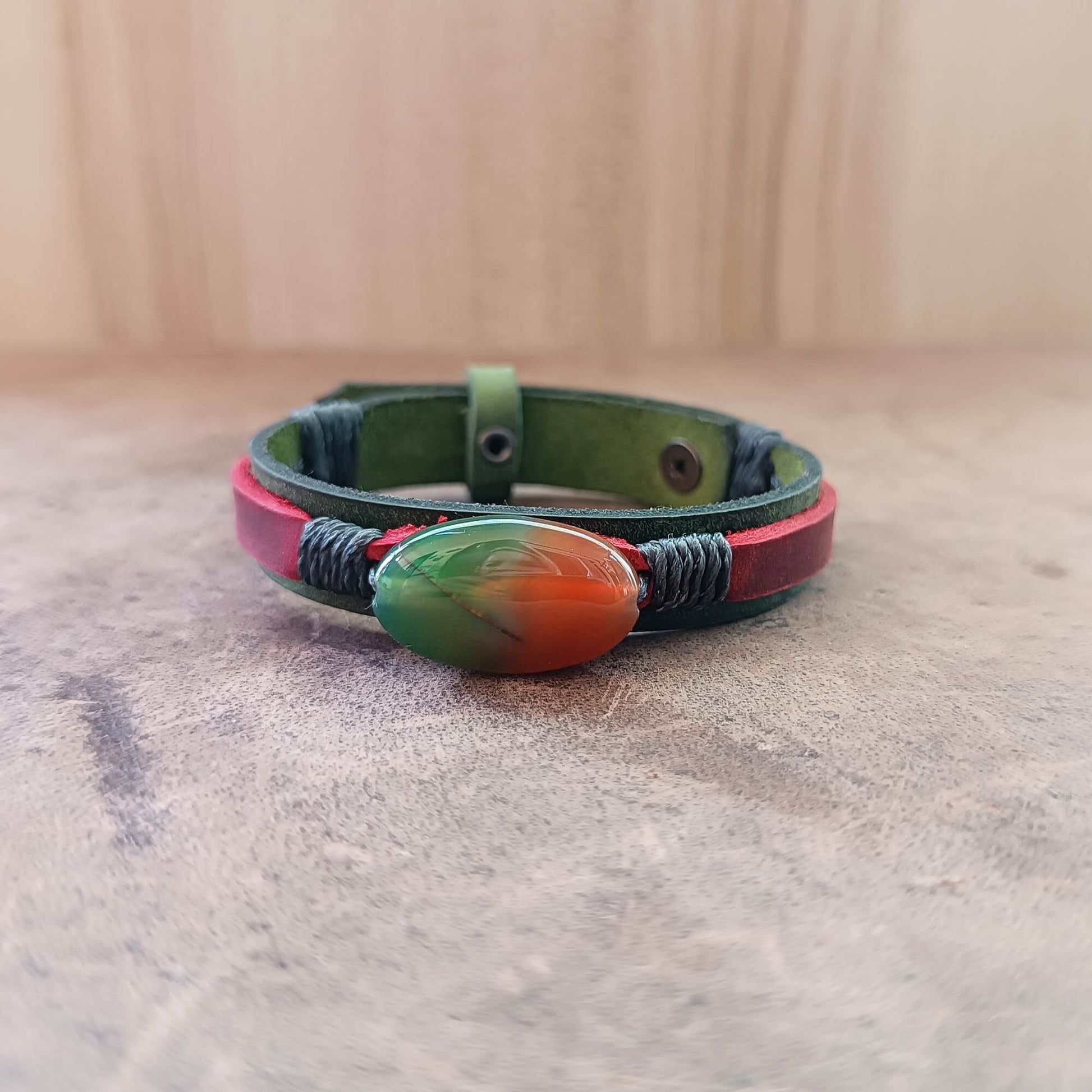 green and red leather Bracelet with a colorful peacock agate bead on  neutral background
