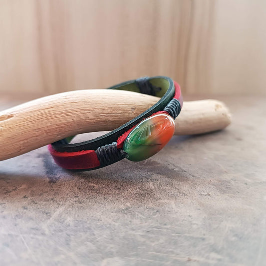 green and red leather Bracelet with a colorful peacock agate bead on a wooden stick against a neutral background