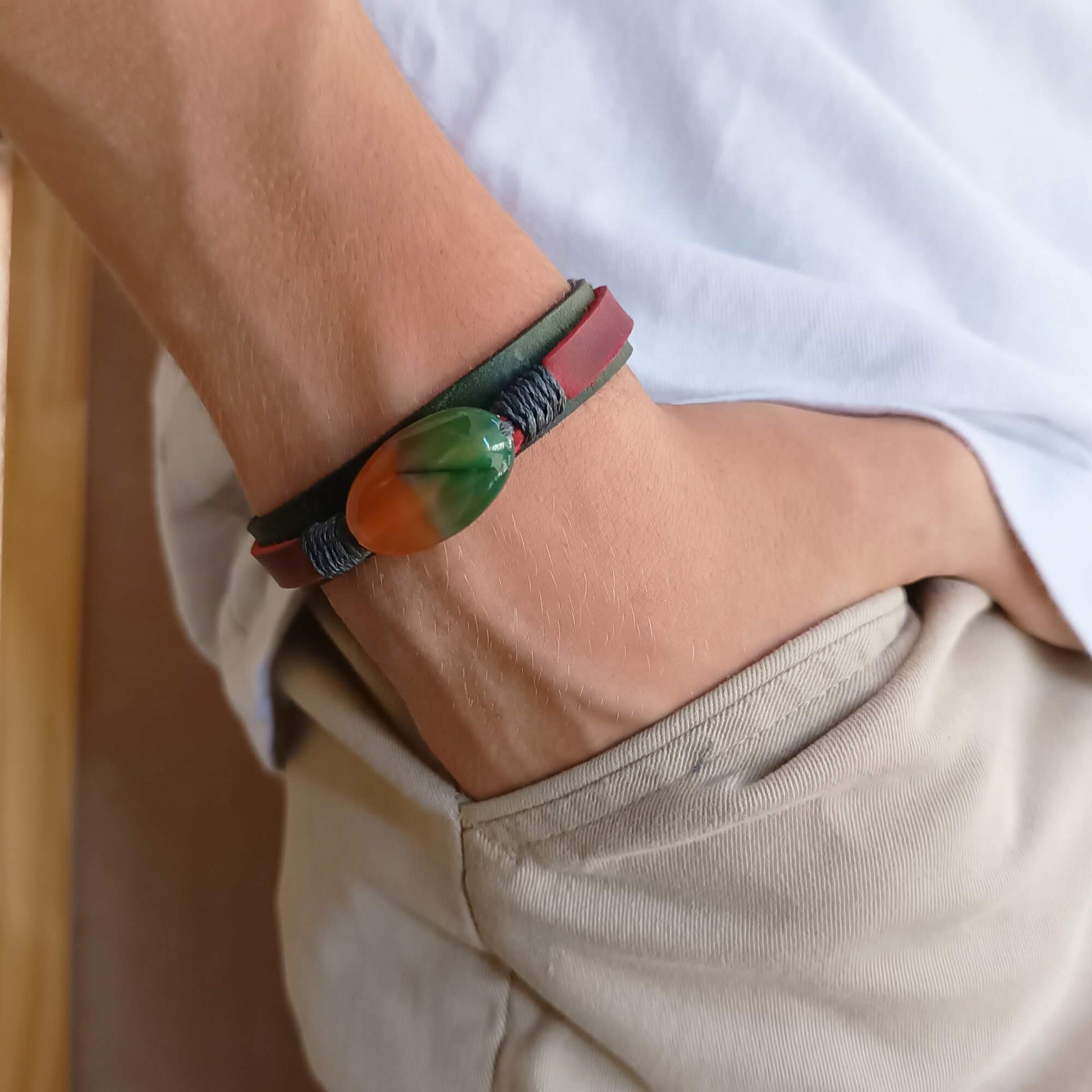 Close-up of a wrist wearing a green and red leather Bracelet with a colorful peacock agate bead