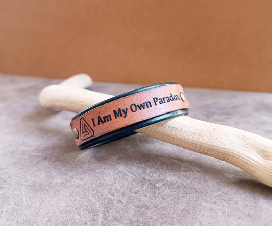 Brown leather bracelet with text on a wooden stick against a beige background