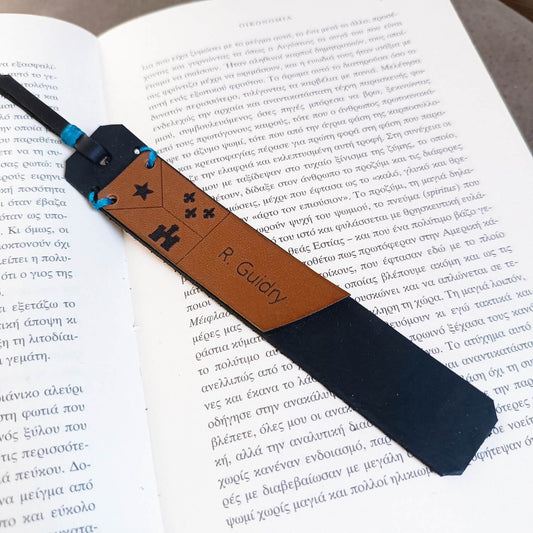 A personalized Cajun leather bookmark with an Acadian flag, placed on an open book.