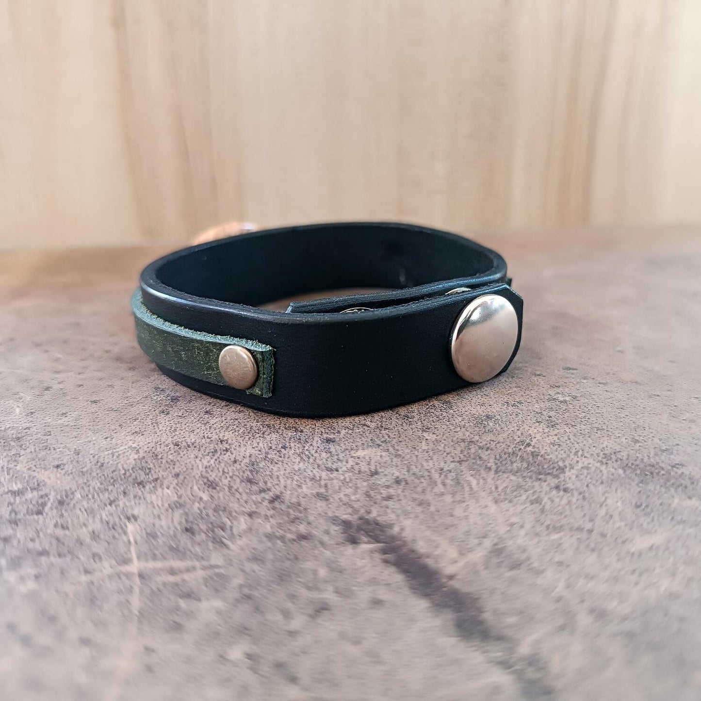 Black leather bracelet with silver buttons on a textured surface