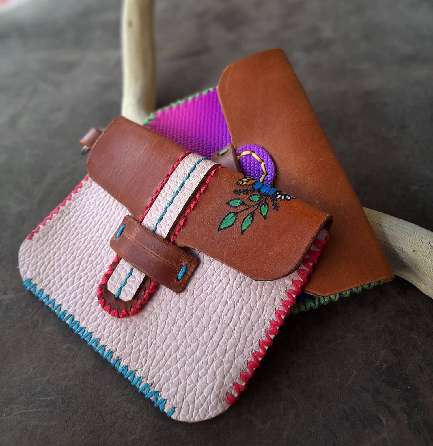 Small leather pouch with colorful stitching and embroidery on a dark surface