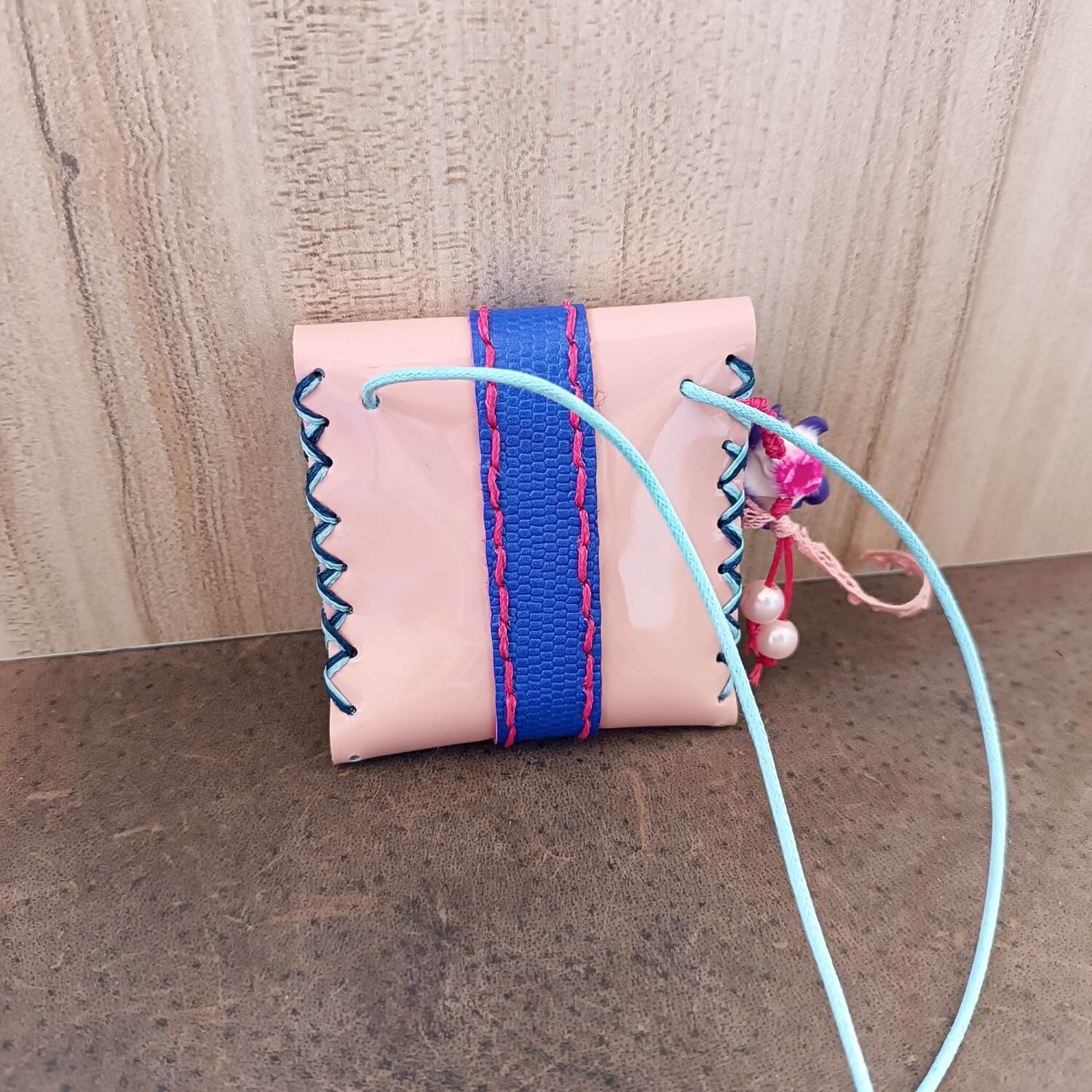 Pink pouch with blue and pink strap on a wooden surface