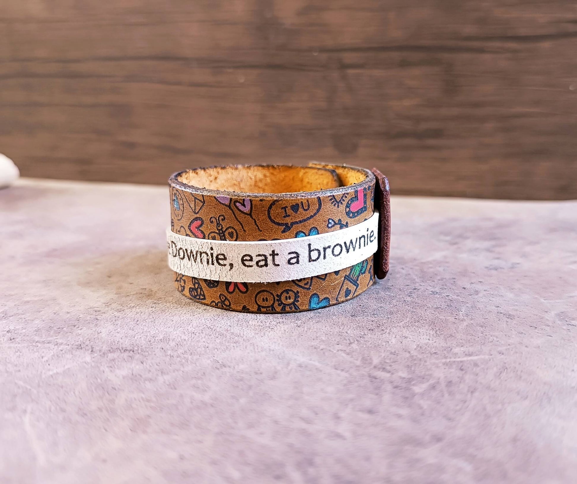 Leather bracelet with patterned band and text on a wooden surface