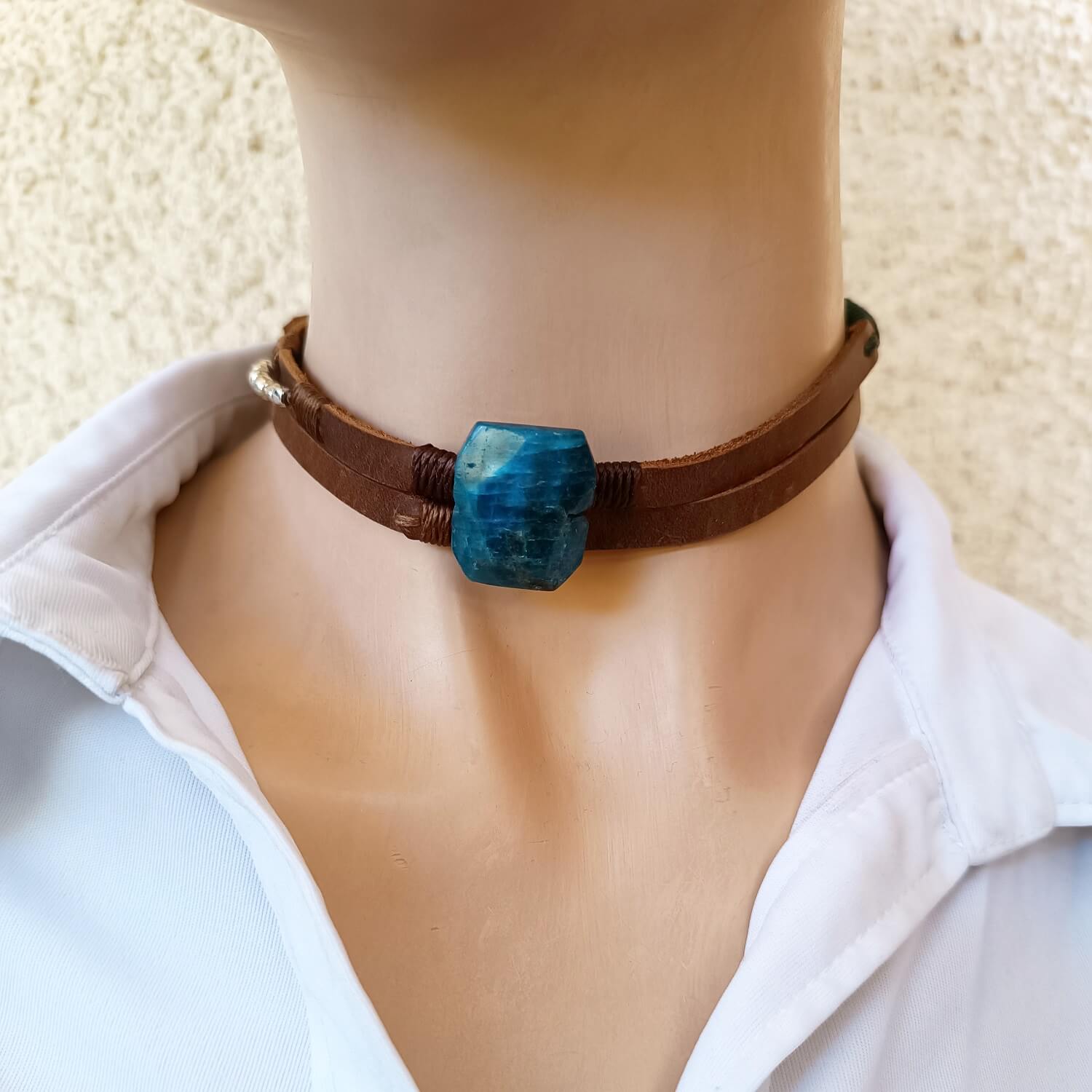 Brown leather choker with a blue stone on a person wearing a white shirt.
