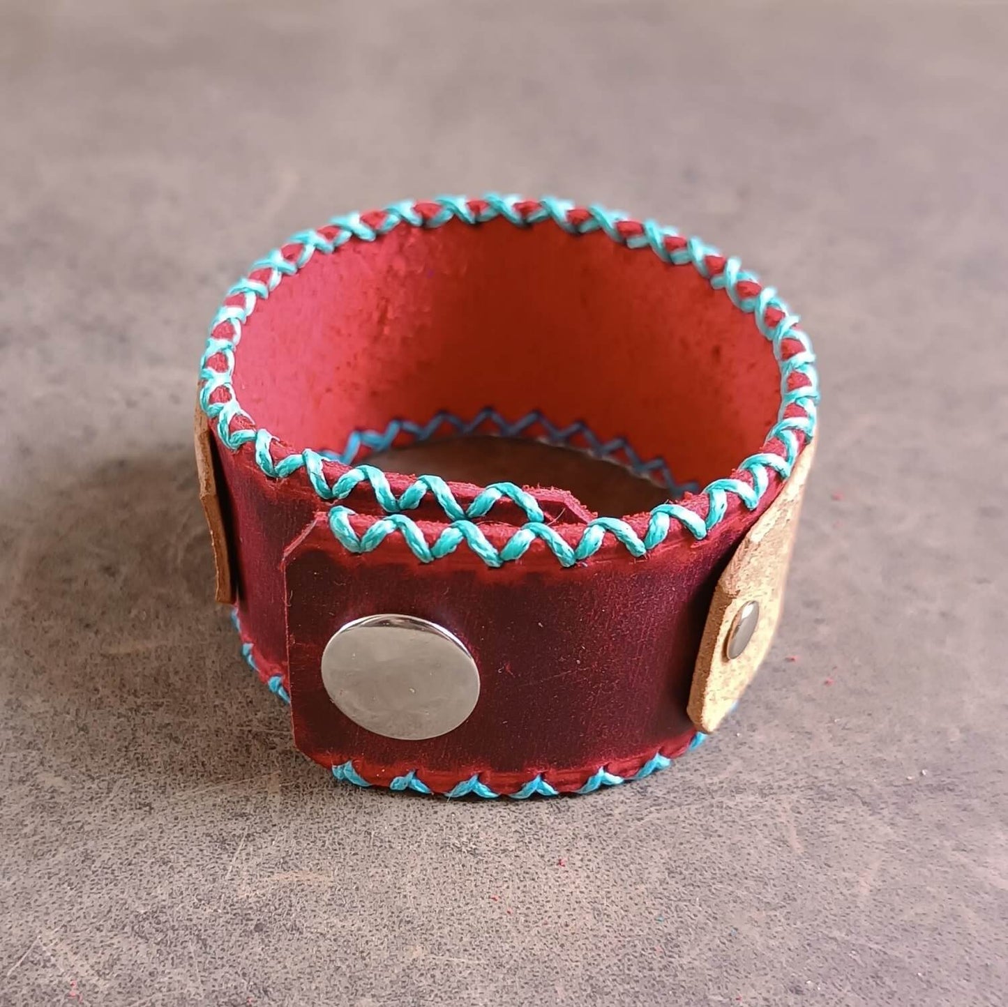 Red leather bracelet with turquoise stitching on a gray background showcasing closure