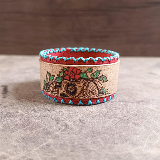 A floral sugar skull leather cuff with a blood red base and beige top layer, featuring turquoise thread and a stainless steel clasp.