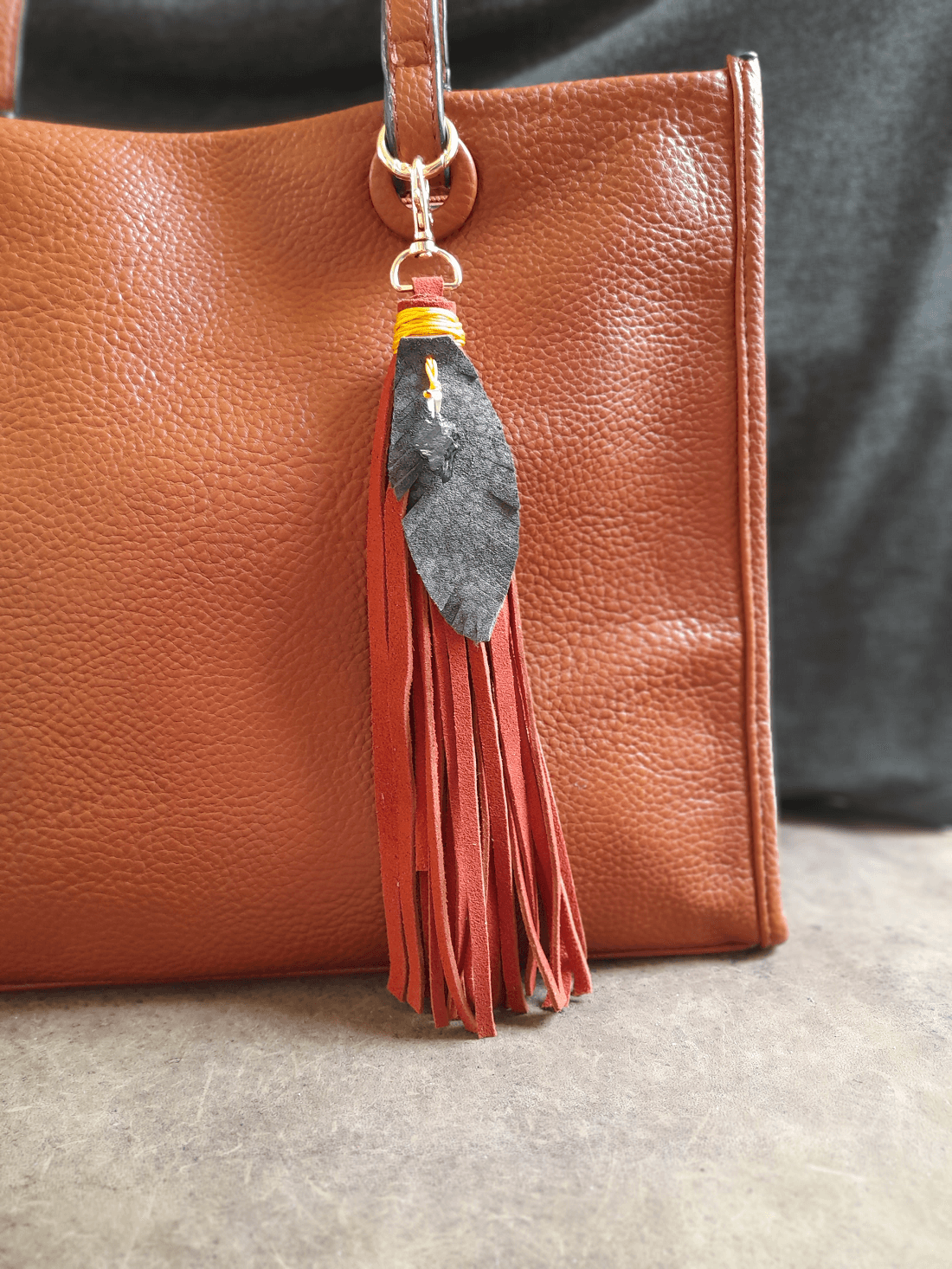 Brown leather handbag with a tassel keychain on a neutral background