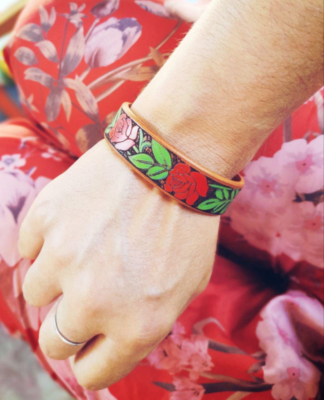 the red rose vine leather cuff bracelet worn on a woman's wrist with red floral outfit.