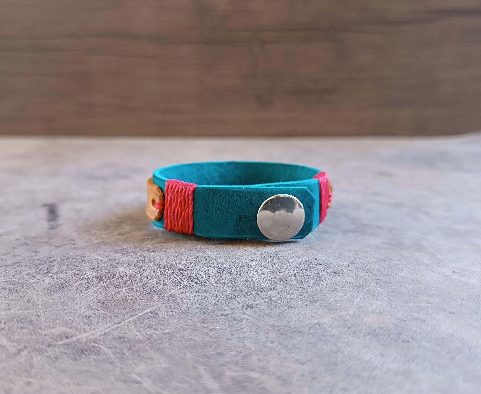 Turquoise bracelet with colorful accents and a silver button on a wooden surface